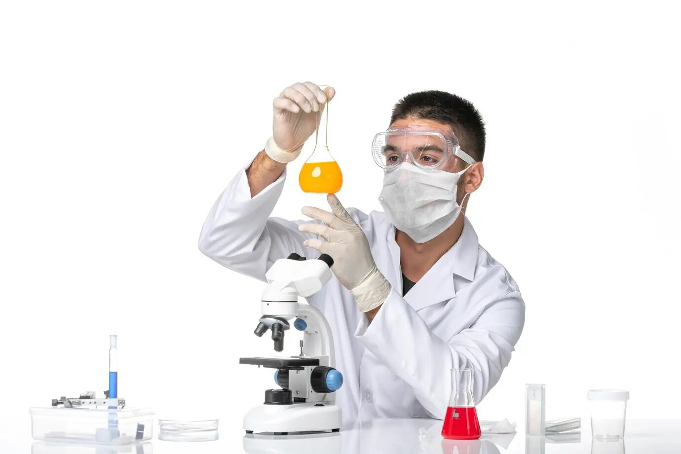 Vista frontal de un médico hombre con traje médico blanco y mascarilla debido a la covid, trabajando con soluciones sobre fondo blanco.