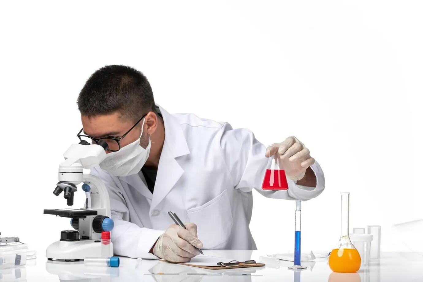 Vista frontal de un doctor masculino con traje médico blanco y mascarilla, sosteniendo una solución roja sobre un escritorio blanco.